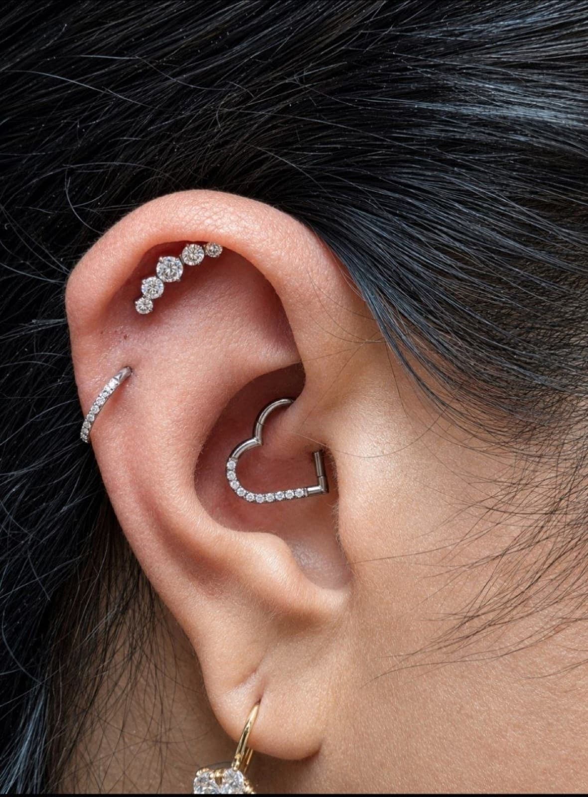 Close-up of a client's ear with daith, helix and lobe piercings styled with silver jewelry